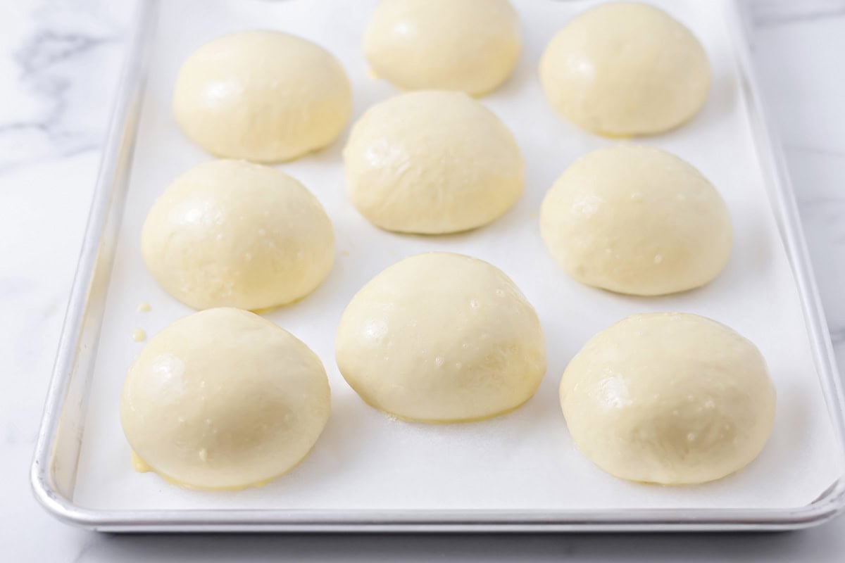 Brioche buns on a lined baking sheet.