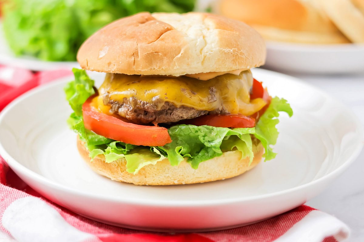 Burgers in the oven on a bun with cheese, lettuce, and tomato.