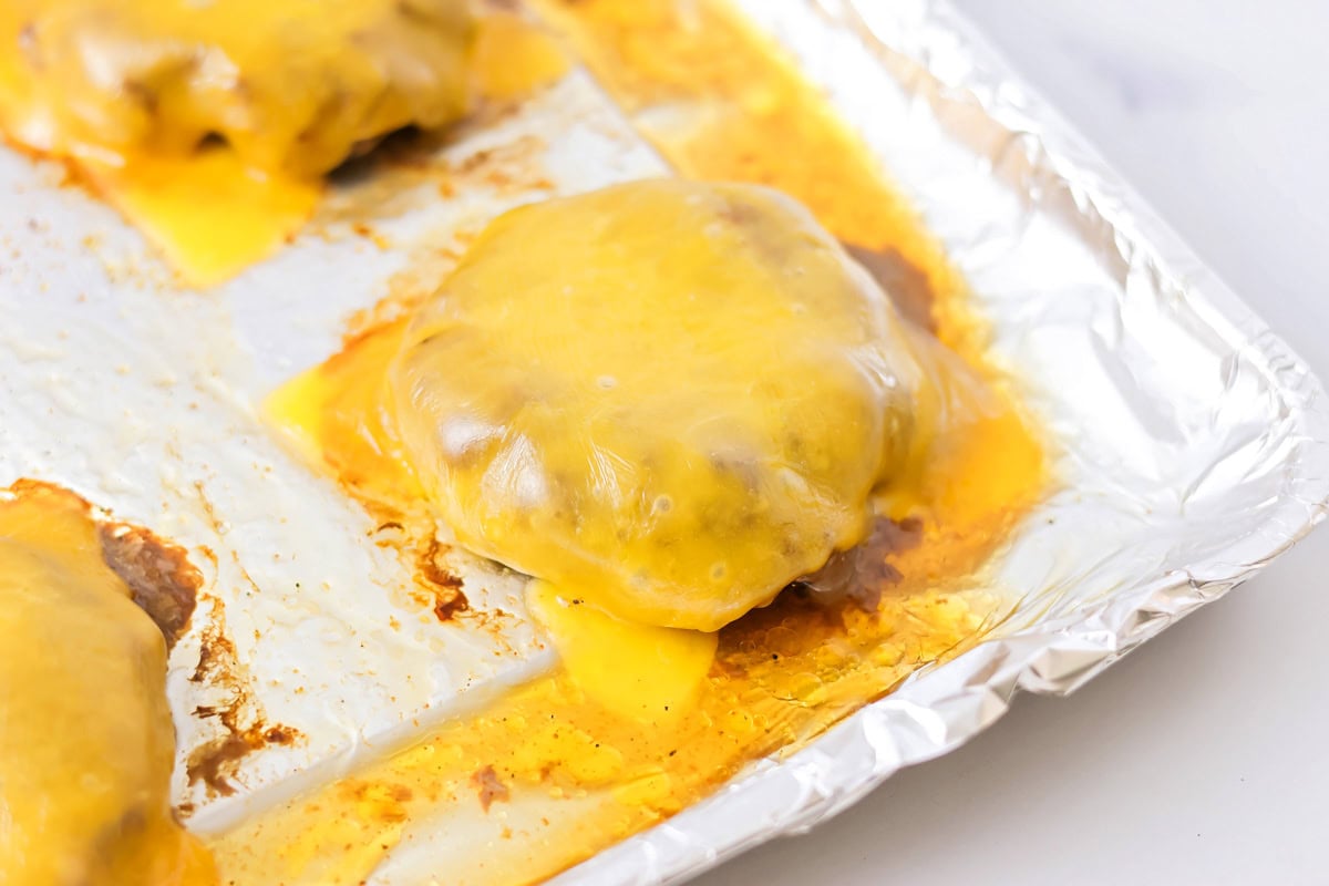Burgers on a lined sheet pan covered in melted cheese.