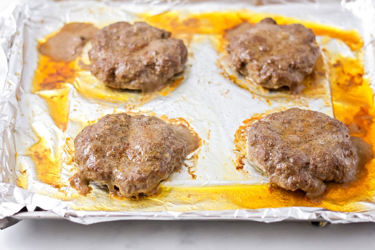 Baked burgers on a lined sheet pan.