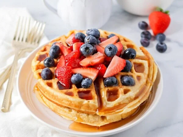 Buttermilk waffles stacked on top of each other with berries on top.
