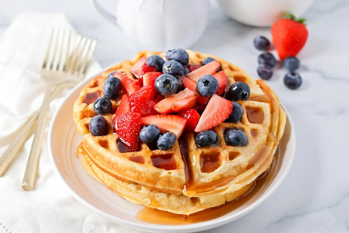 There's nothing better than big, fluffy buttermilk waffles first thing in the morning! This will be your new favorite breakfast recipe!! Stack of buttermilk waffles topped with berries and syrup.