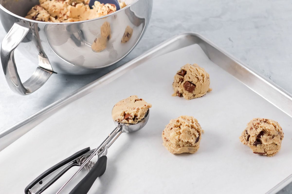 Scooping dough balls onto a lined cookie sheet.