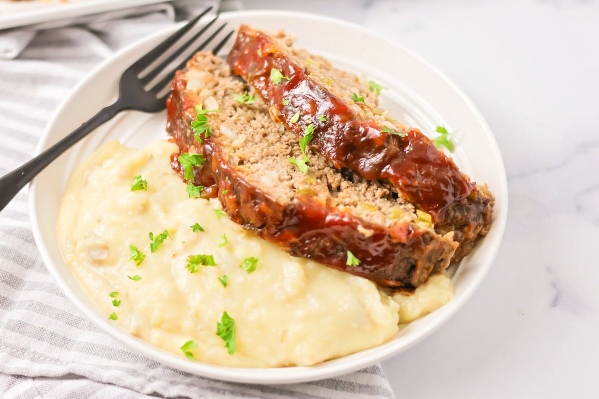 Two slices of Cracker Barrel meatloaf served with mashed potatoes on a white plate.