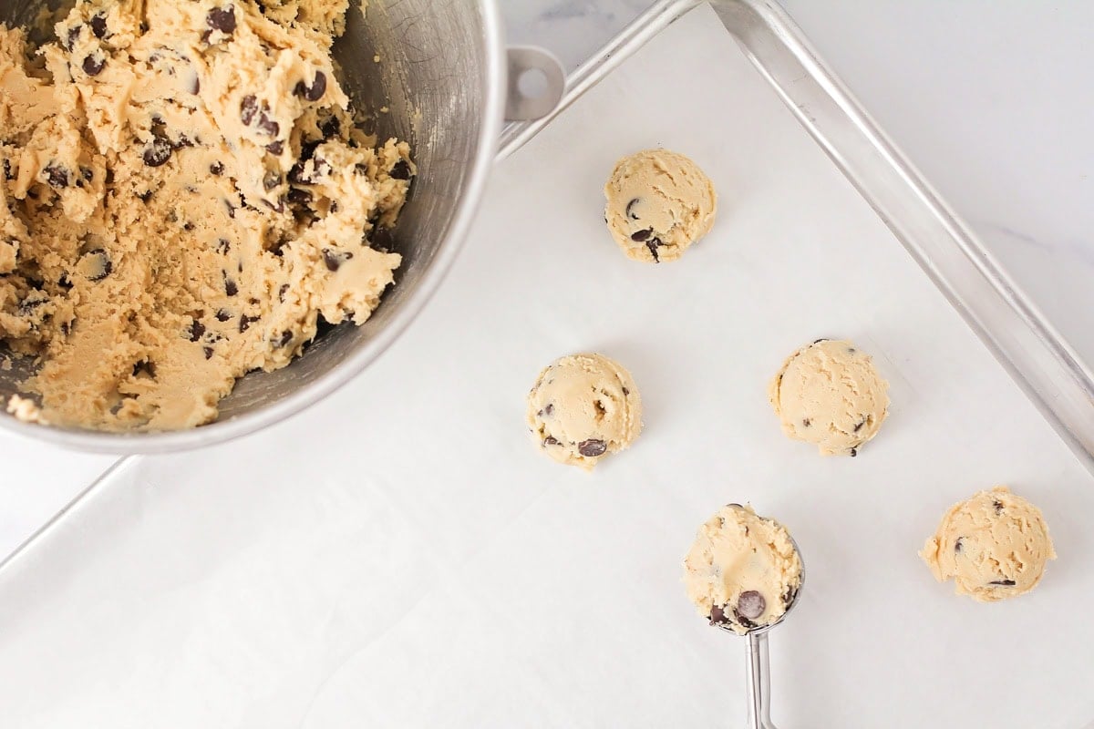 Scooping cookie dough balls on the lined baking sheet.