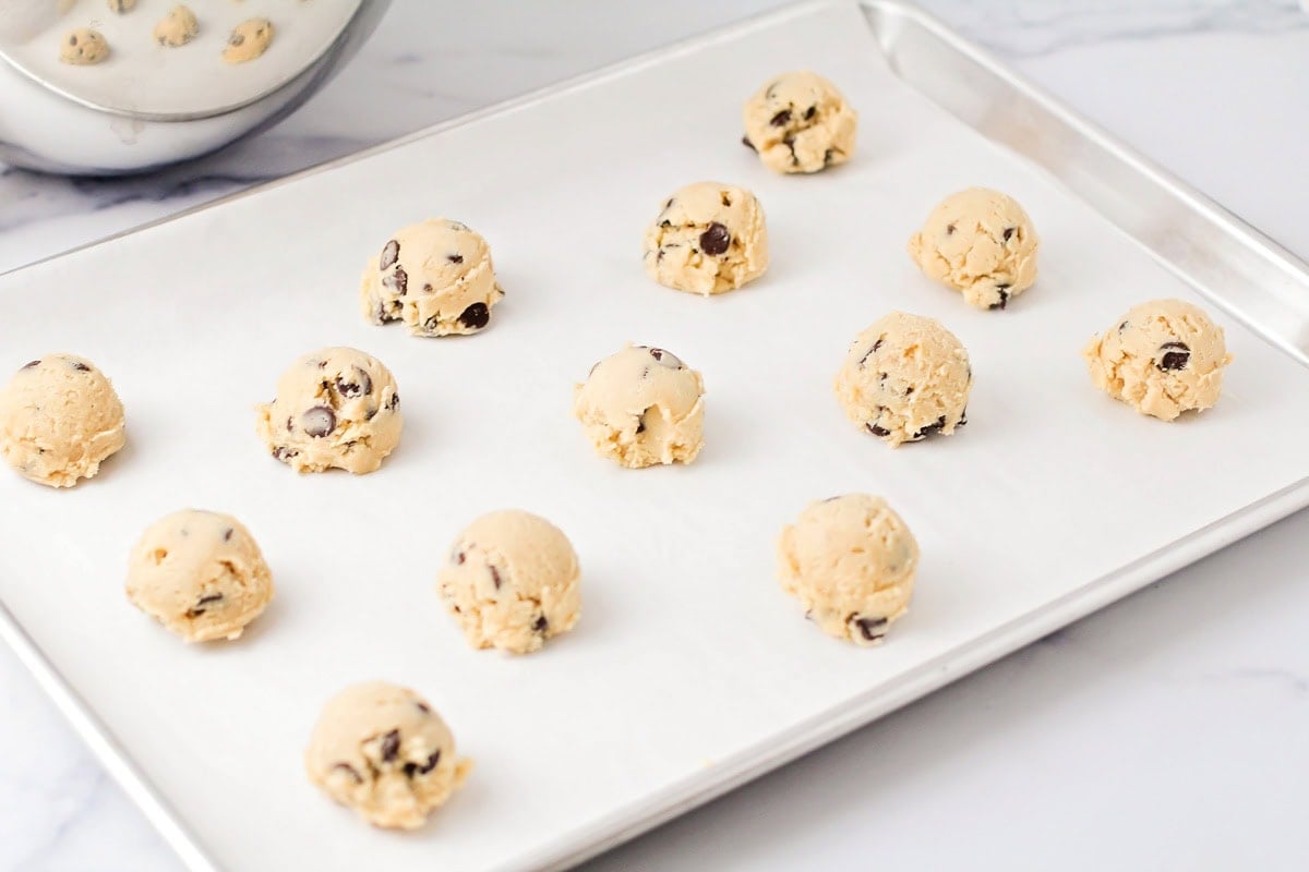 Cookie dough balls on a lined baking sheet.
