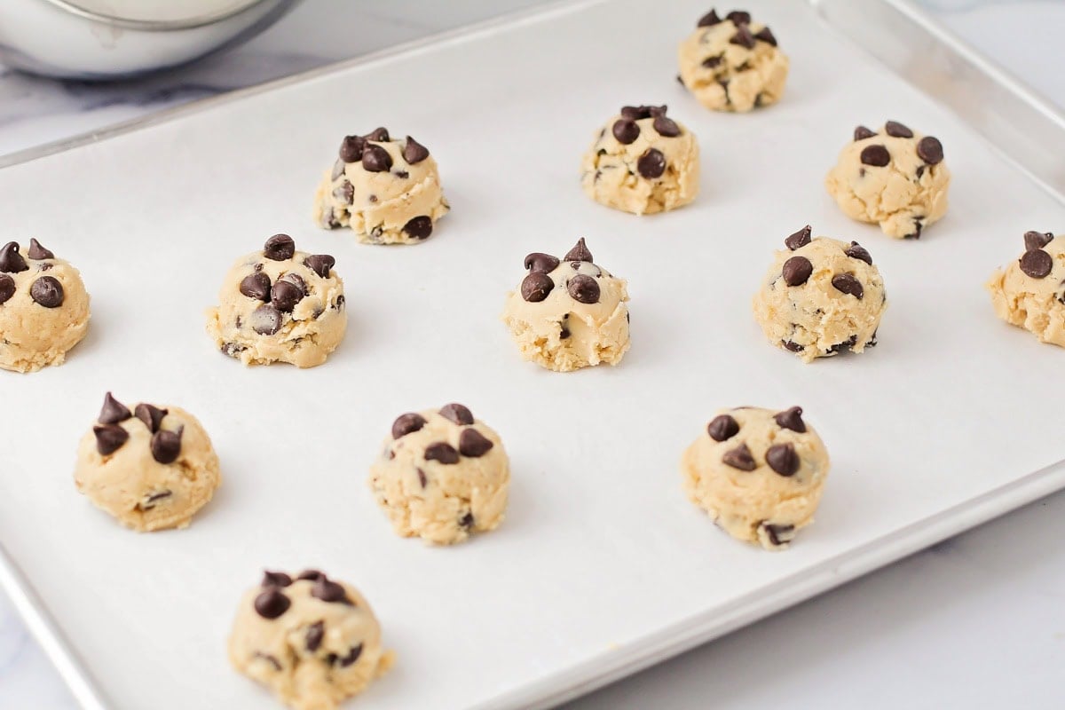 Eggless chocolate chip cookies dough balls on a lined baking sheet.