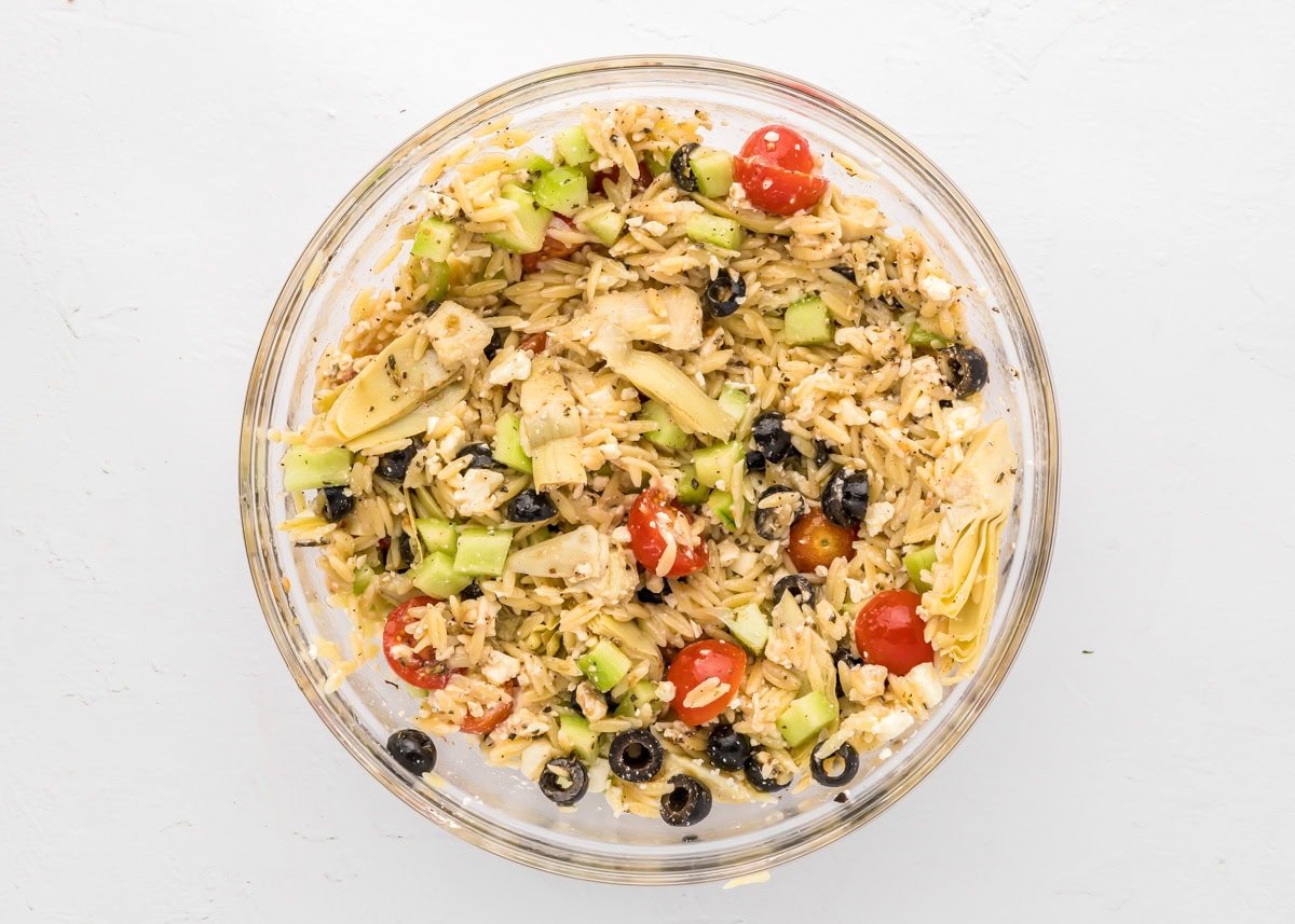 A mixed greek orzo pasta salad in a glass bowl.