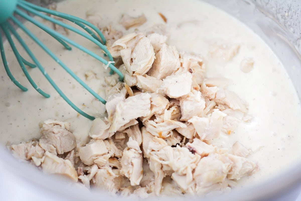 Adding chicken chunks to a pot of gravy.