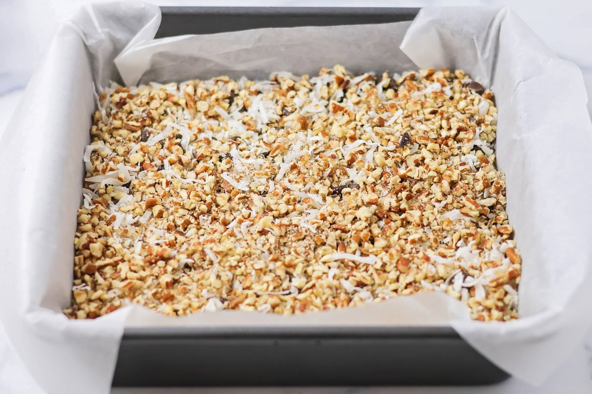 Sprinkling coconut and pecans on top of the chocolate chips.