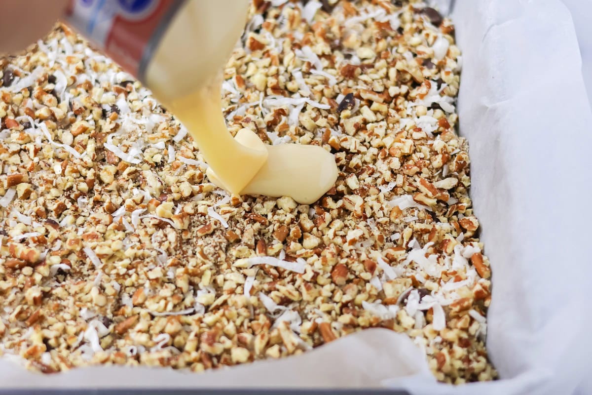 Pouring sweetened condensed milk over the Hello Dolly bars.