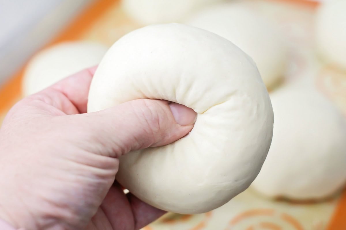 Shaping the dough balls into bagels by punching a hole in the center with your thumb.