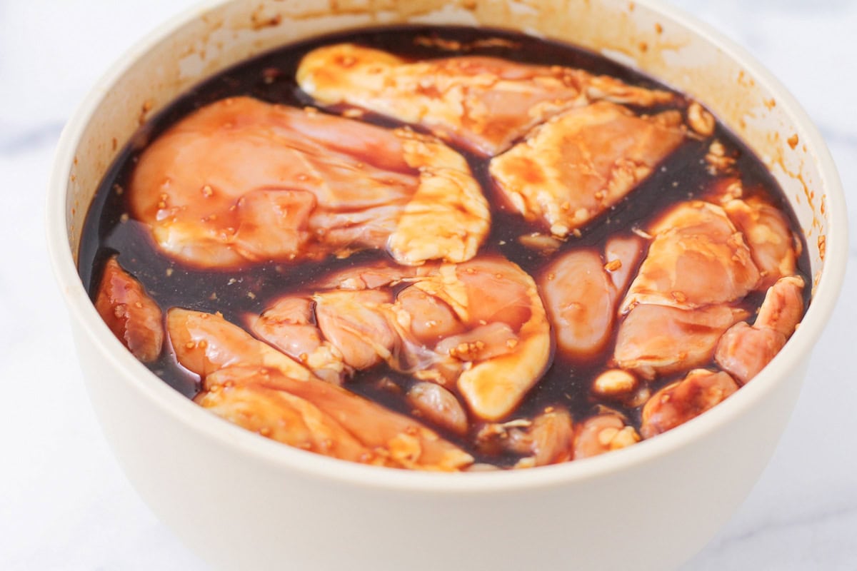 Grilled Huli Huli chicken is juicy, smoky, and glazed with a sweet and tangy Hawaiian-style marinade! Serve it alone or on rice or noodles. Marinating chicken thighs in a bowl.