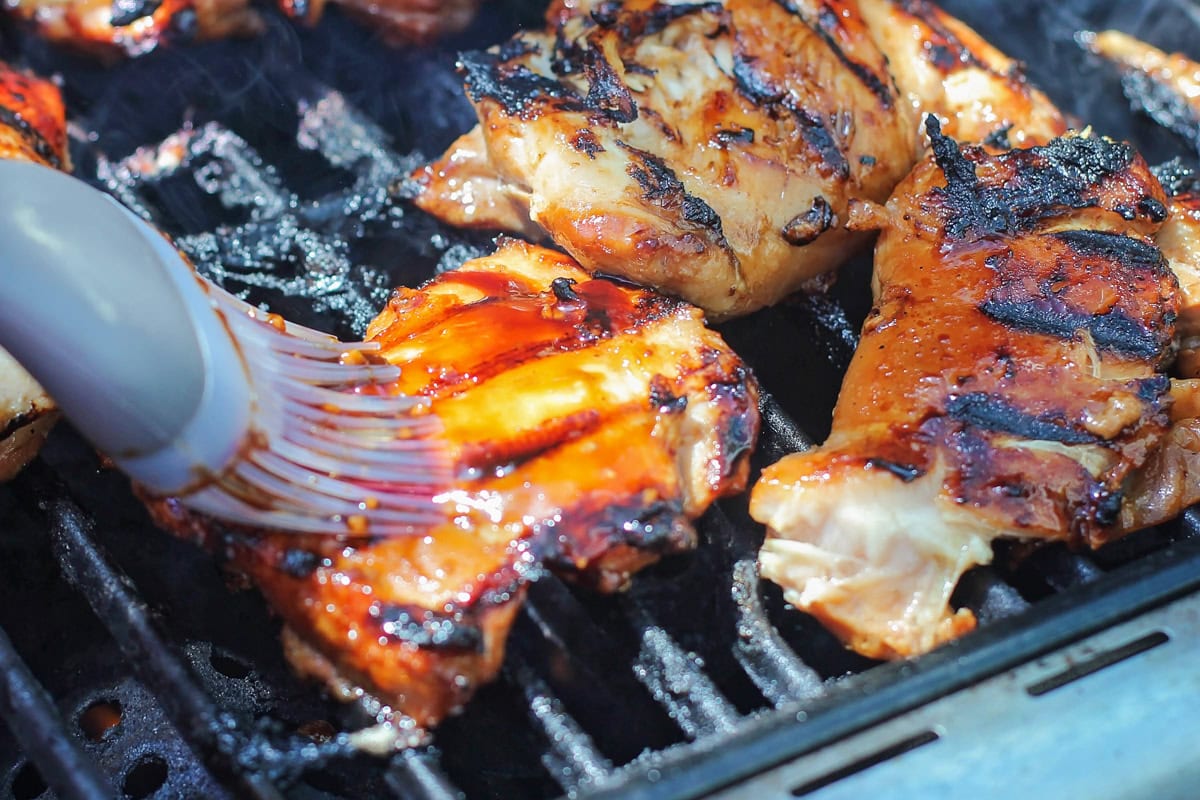 Grilled Huli Huli chicken is juicy, smoky, and glazed with a sweet and tangy Hawaiian-style marinade! Serve it alone or on rice or noodles. Basting huli huli chicken on a grill.