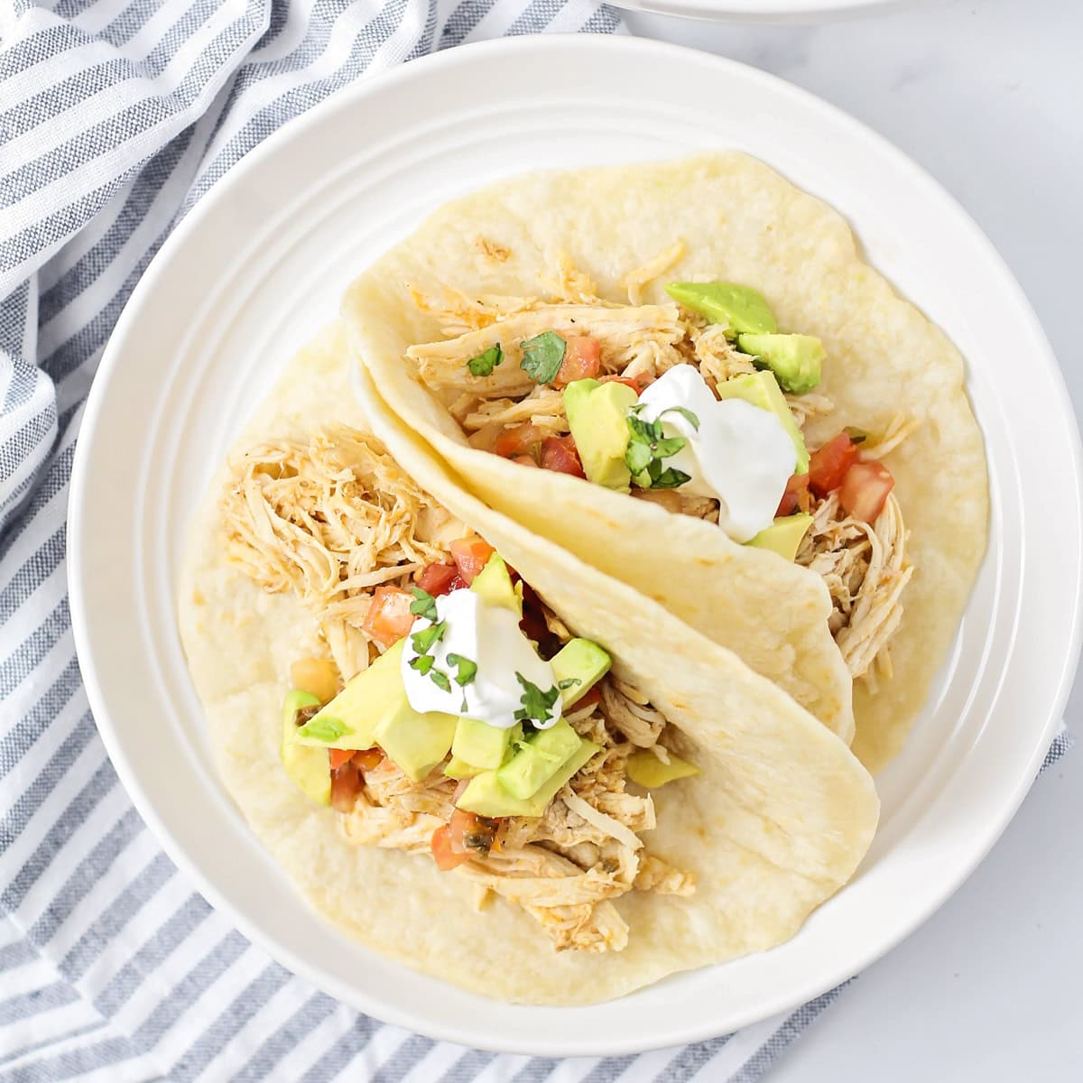 A top view of two instant pot chicken tacos topped with fresh pico, avocado, and sour cream.