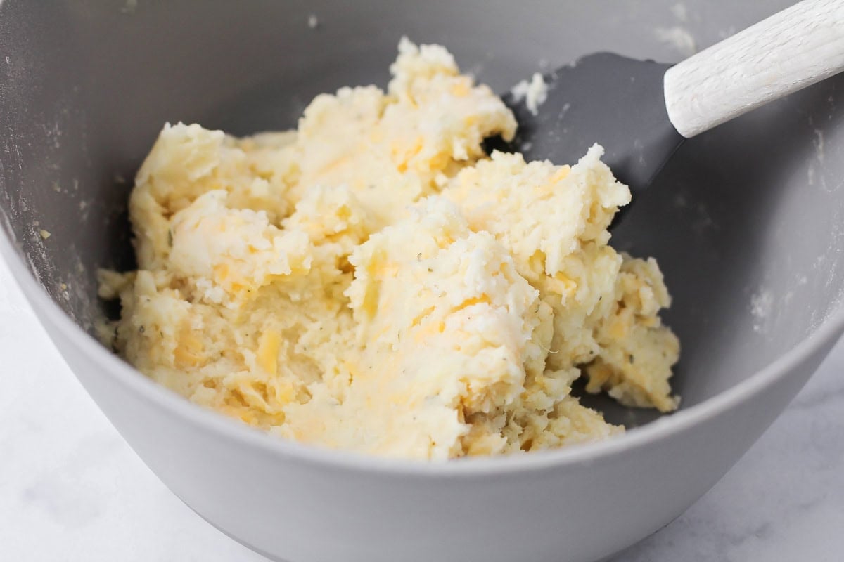 Mixing mashed potatoes and cheese in a bowl.