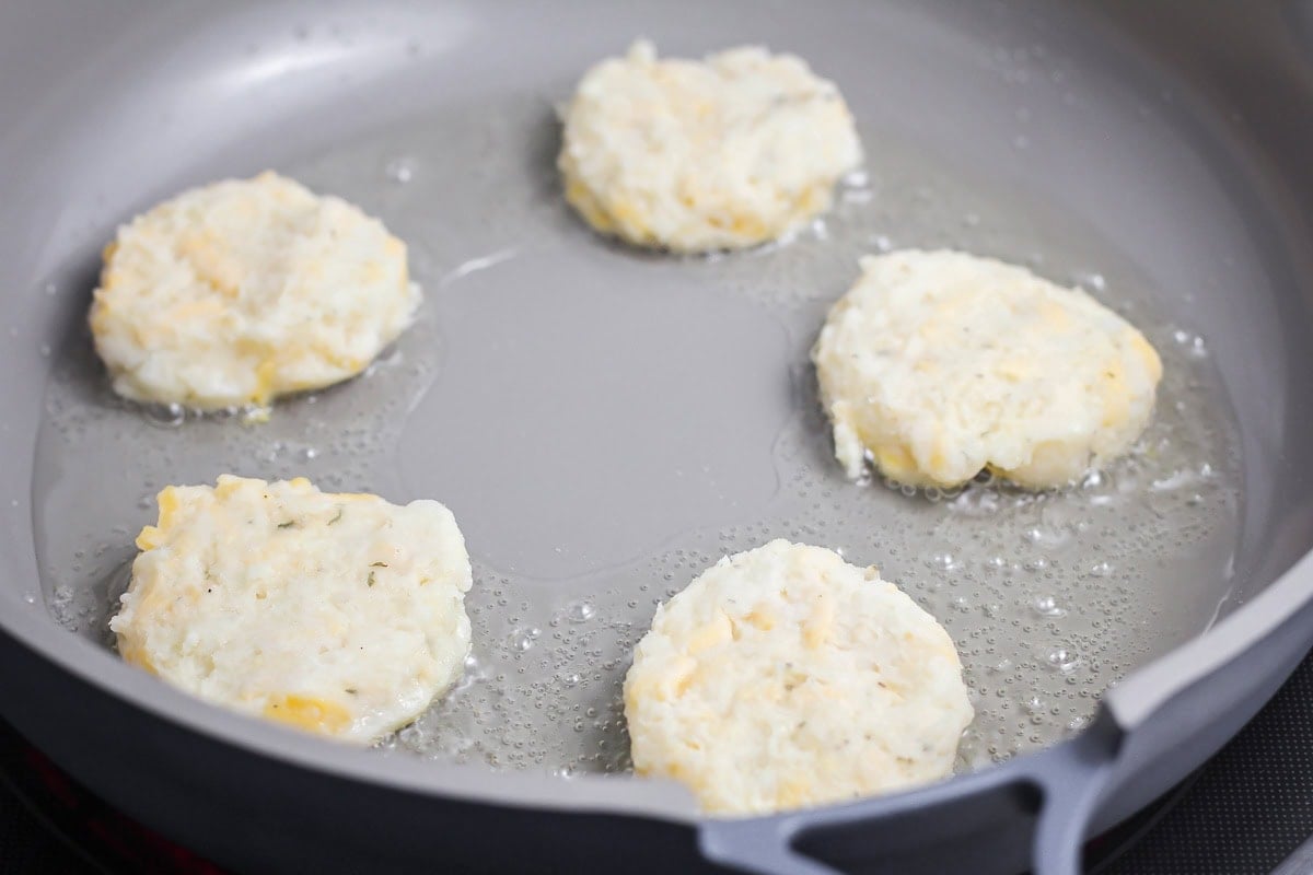 Pancake patties cooking in a skillet of oil.