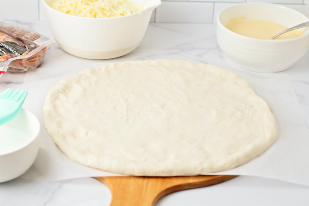 This easy-to-make pretzel crust pizza has an irresistible cheese sauce and kid-approved flavor that's even better than takeout! Pizza dough and other ingredients on a kitchen counter.