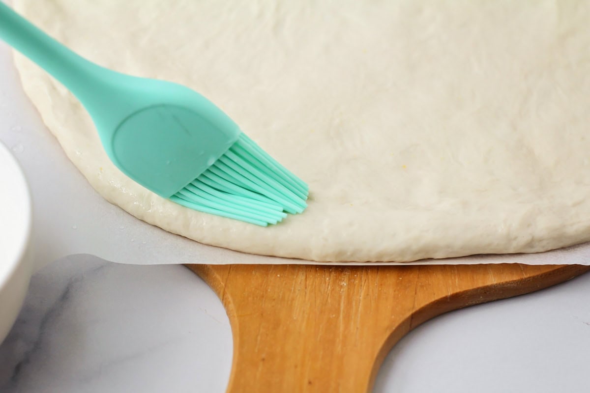 Spreading baking soda mixture onto pizza crust.