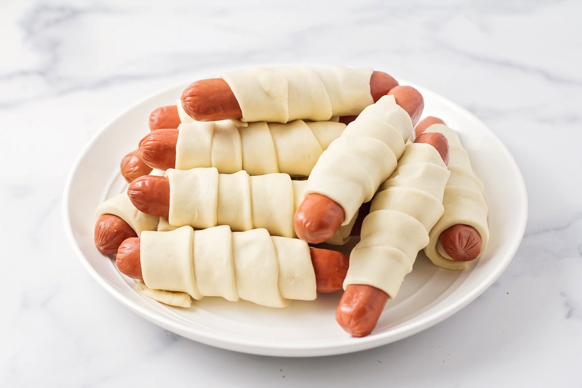 Dough wrapped hotdogs on a white plate.