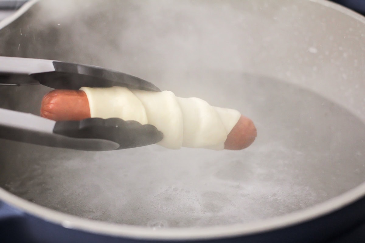 Dipping a dough wrapped hot dog into boiling water.