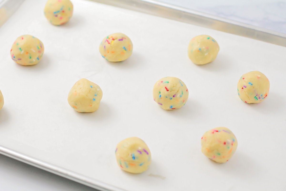 Cookie dough balls on a lined baking sheet.