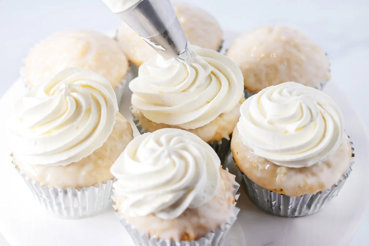 Piping whipped cream onto tres leches cupcakes.