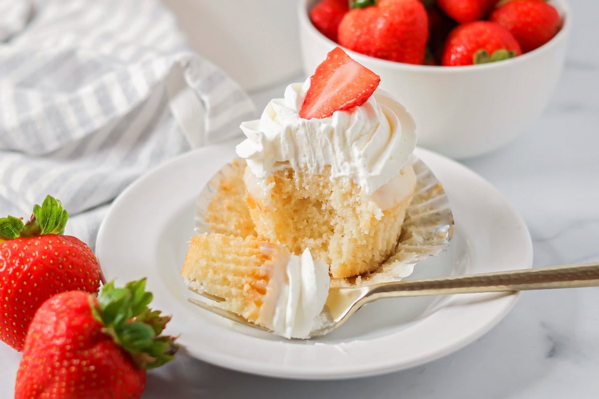Tres leches cupcakes served on a white plate with a bit missing.