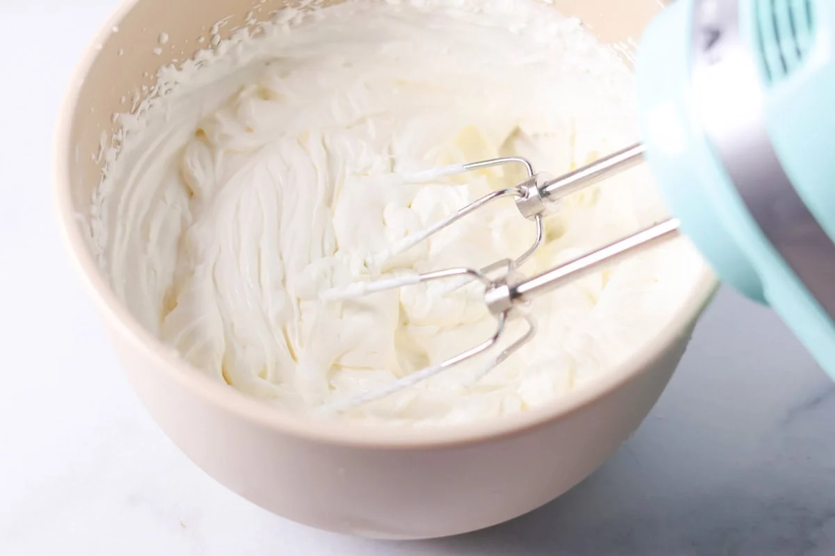Whipping cream in a bowl with a hand mixer.