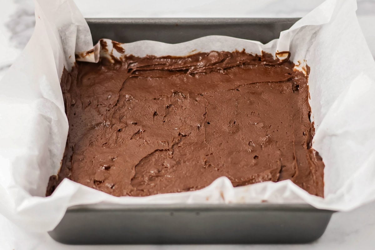 Brownie batter in a lined baking pan.
