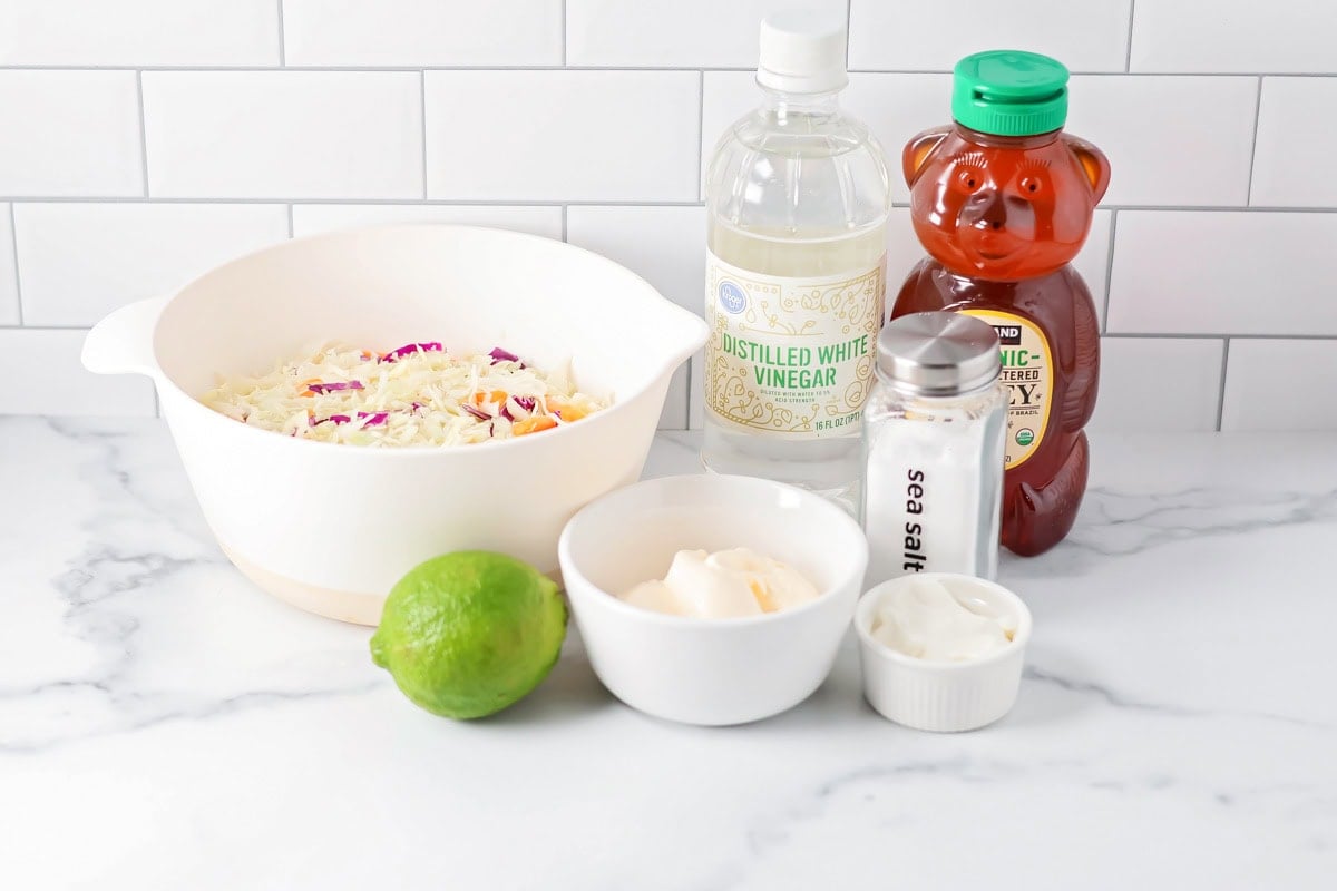 This flaky fish tacos recipe with creamy slaw is ready in just 30 minutes – perfect for quick, delicious tacos any night! Ingredients for fish tacos recipe slaw on a kitchen counter.