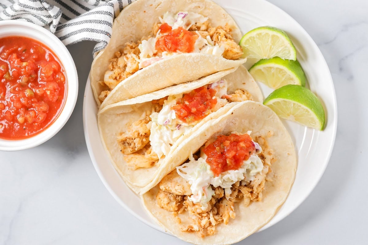 Three fish tacos recipe served with fresh lime slices.