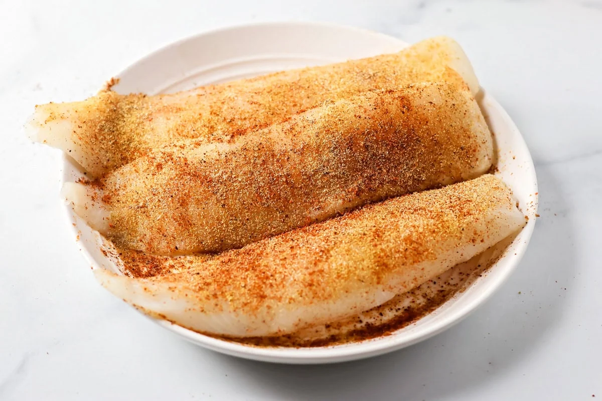 Seasoned fish in a white dish.
