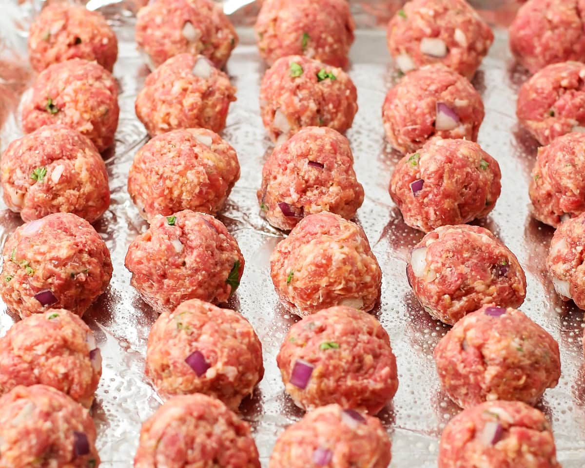 Shaped meatballs on a lined baking sheet.
