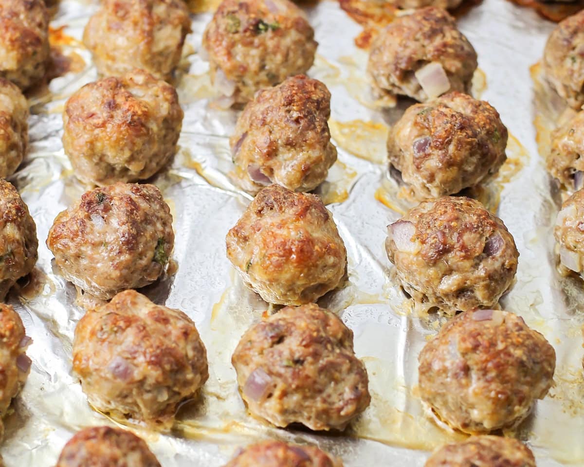 Baked meatballs on a lined baking sheet.