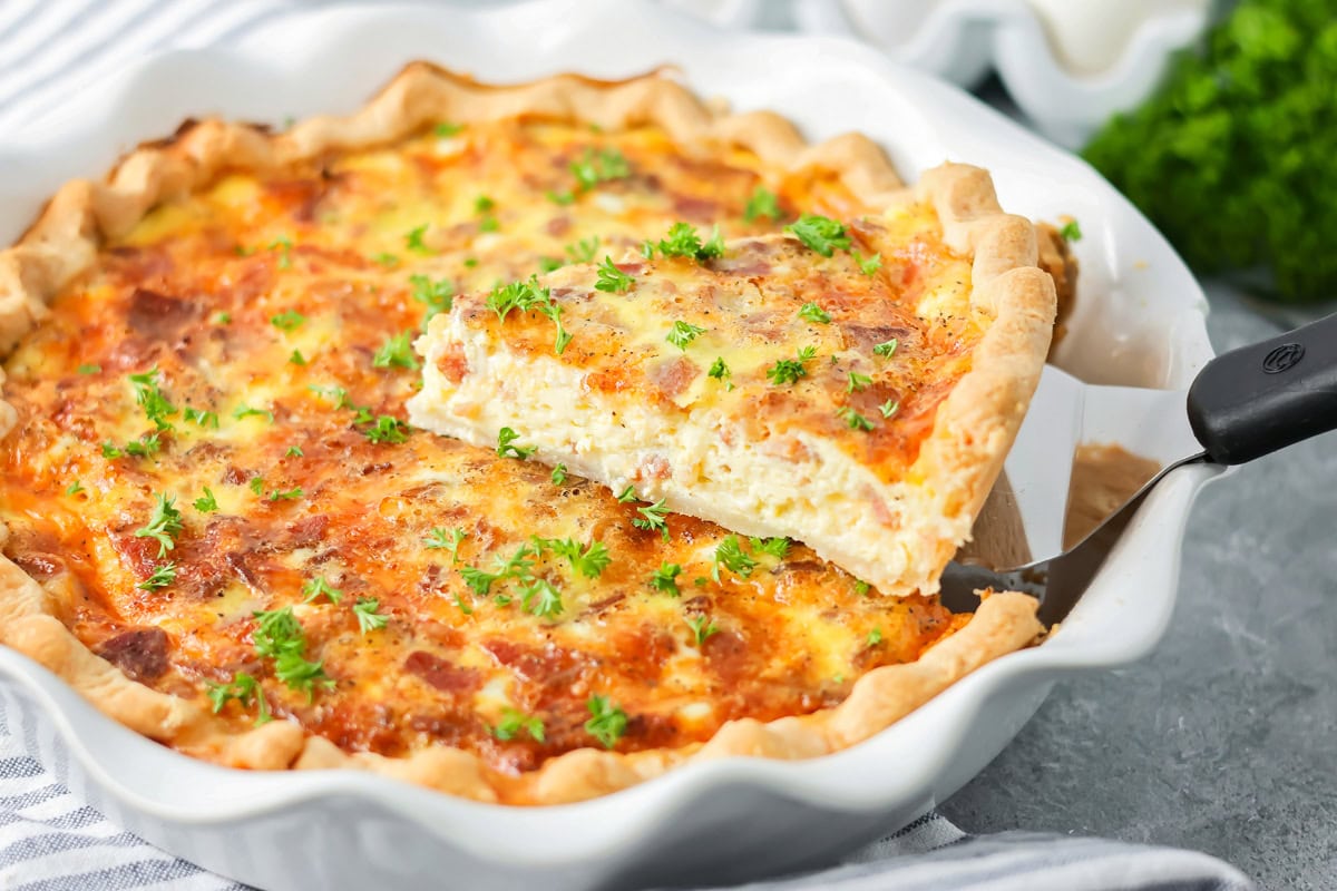 Slice of the easiest and best bacon quiche recipe being taken out of pie dish.