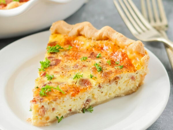 A slice of the best quiche recipe on a white plate.