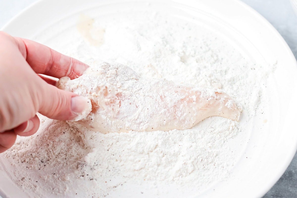 Dipping chicken breasts in a bowl of flour.