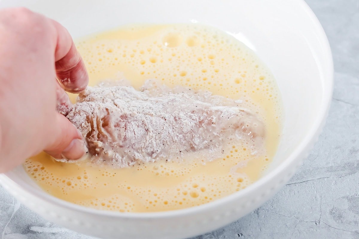 Dipping coated chicken breasts in a bowl of egg mixture.
