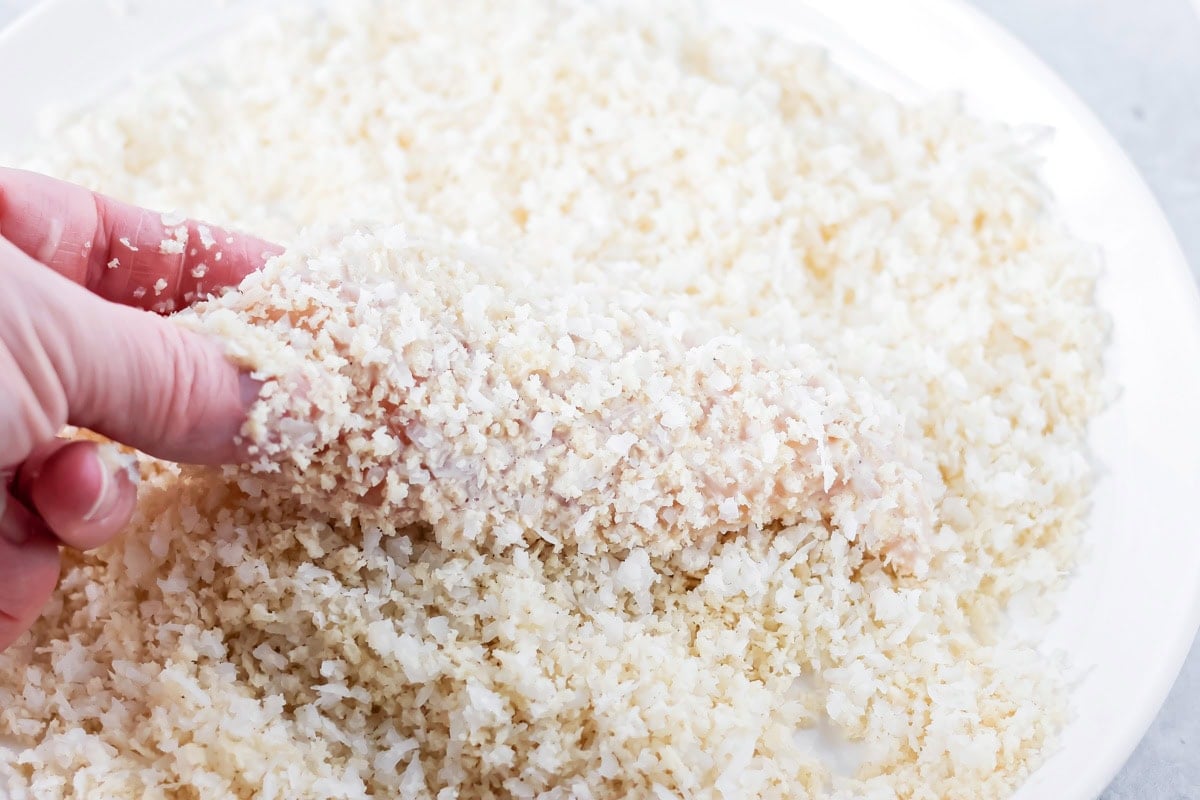 Coating chicken in coconut crumb mixture.