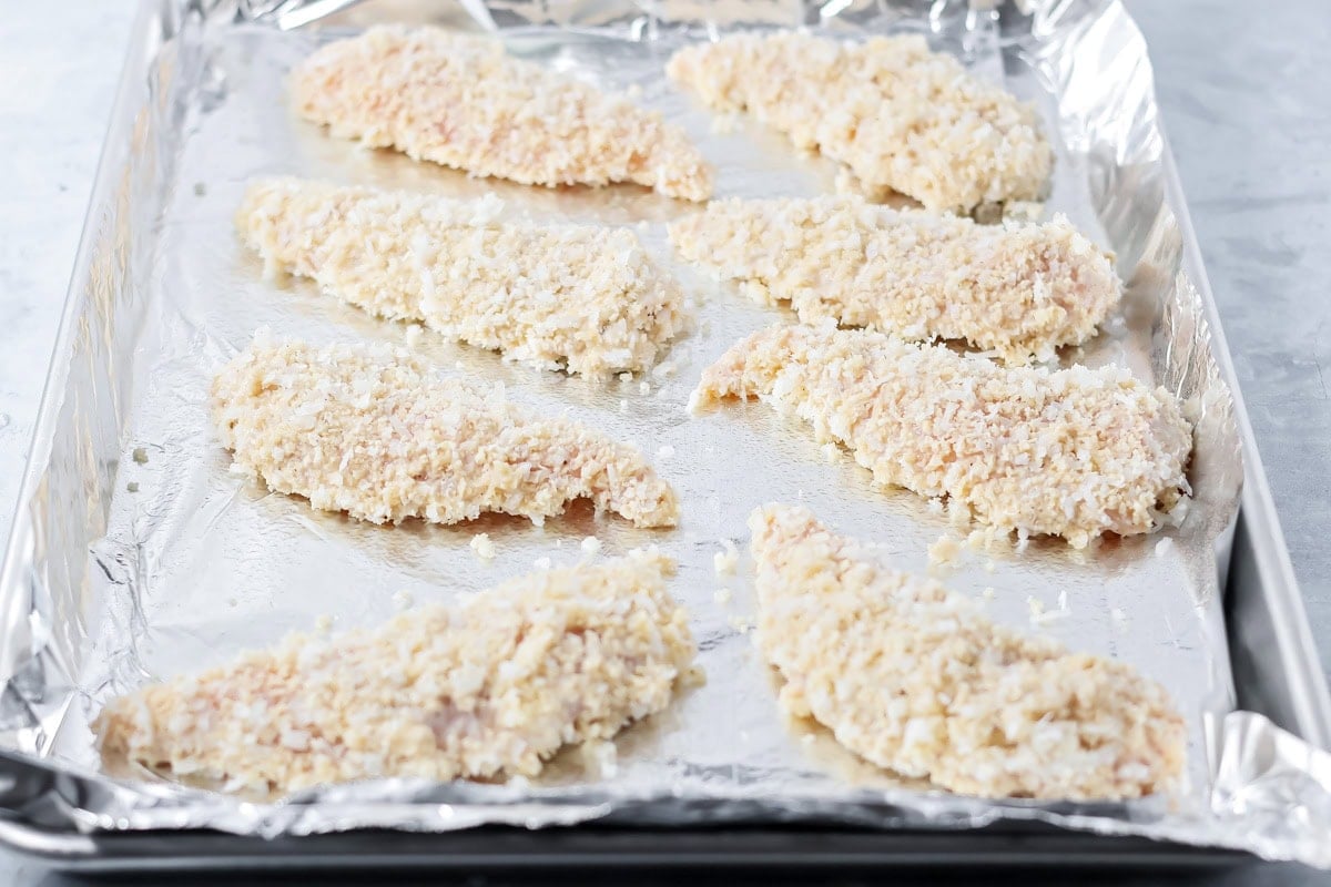 Chicken strips on a lined baking sheet ready to be baked.