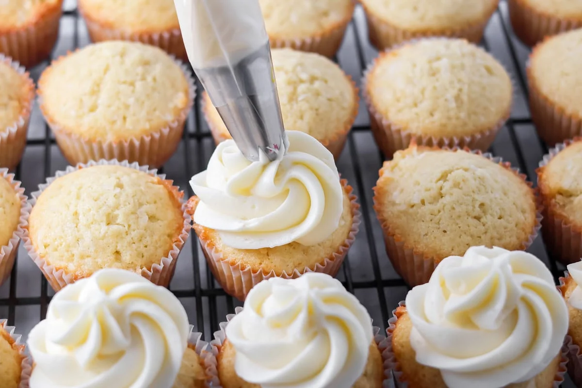 Topping coconut cupcakes with cream cheese frosting.