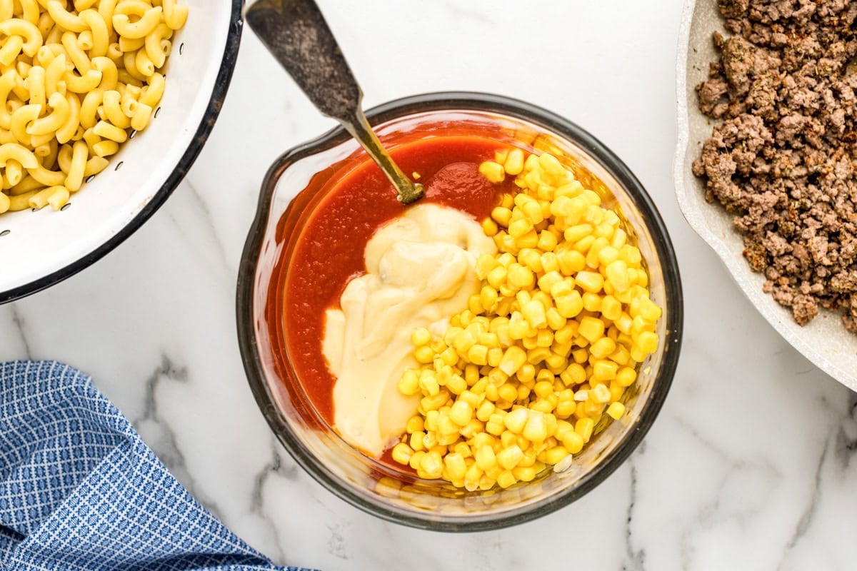 Mixing corn and sauce ingredients in a glass bowl.
