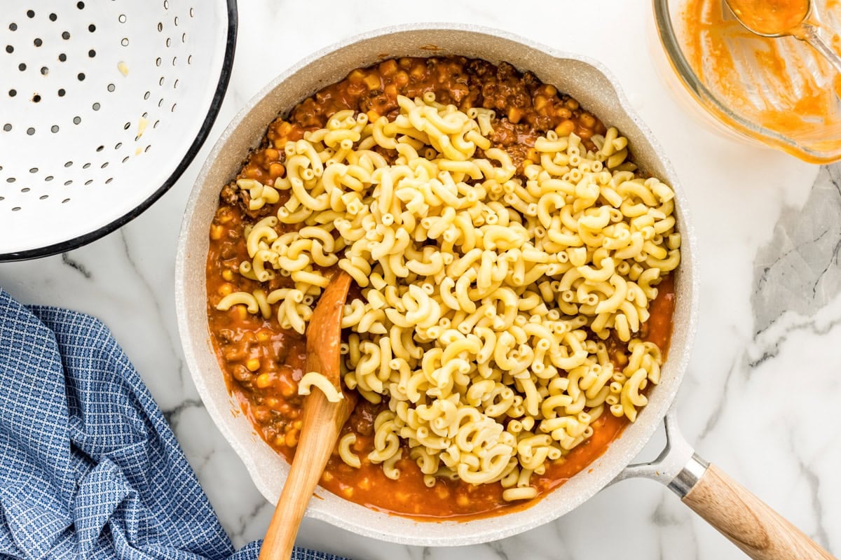 Adding pasta to the meat and sauce.