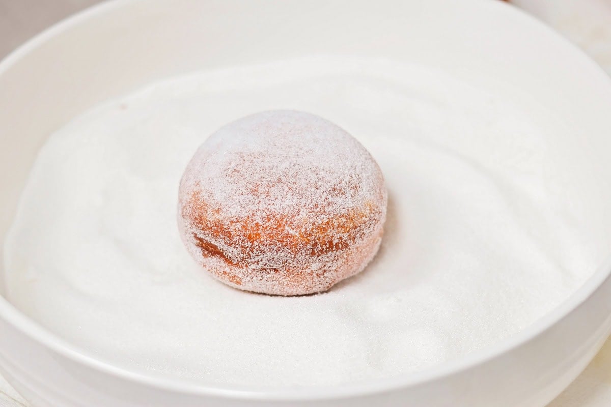 Coating a fried donut in sugar.