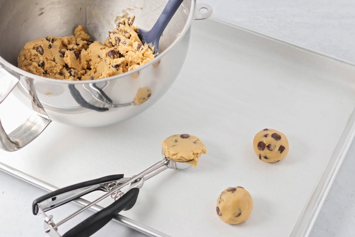 Scooping chocolate chips onto a lined baking sheet.