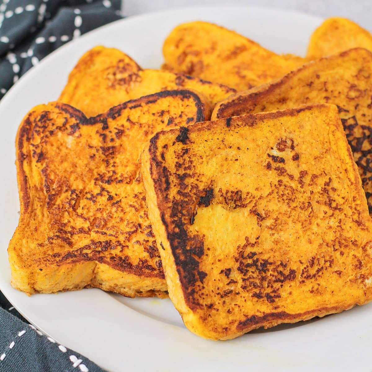 Infused with warm spices and pumpkin, this quick and easy pumpkin French toast transforms breakfast into a cozy, decadent fall favorite! Slices of pumpkin french toast on a white plate.
