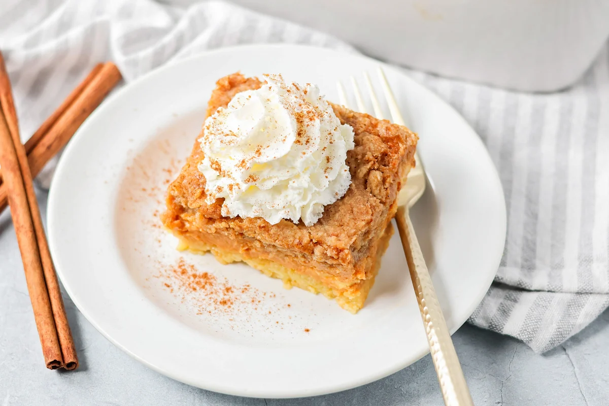 These pumpkin pie bars use a cake mix shortcut to create a fluffy, pumpkin-spiced treat that's perfect for sharing! Pumpkin pie bars slice on a white plate topped with whipped cream.