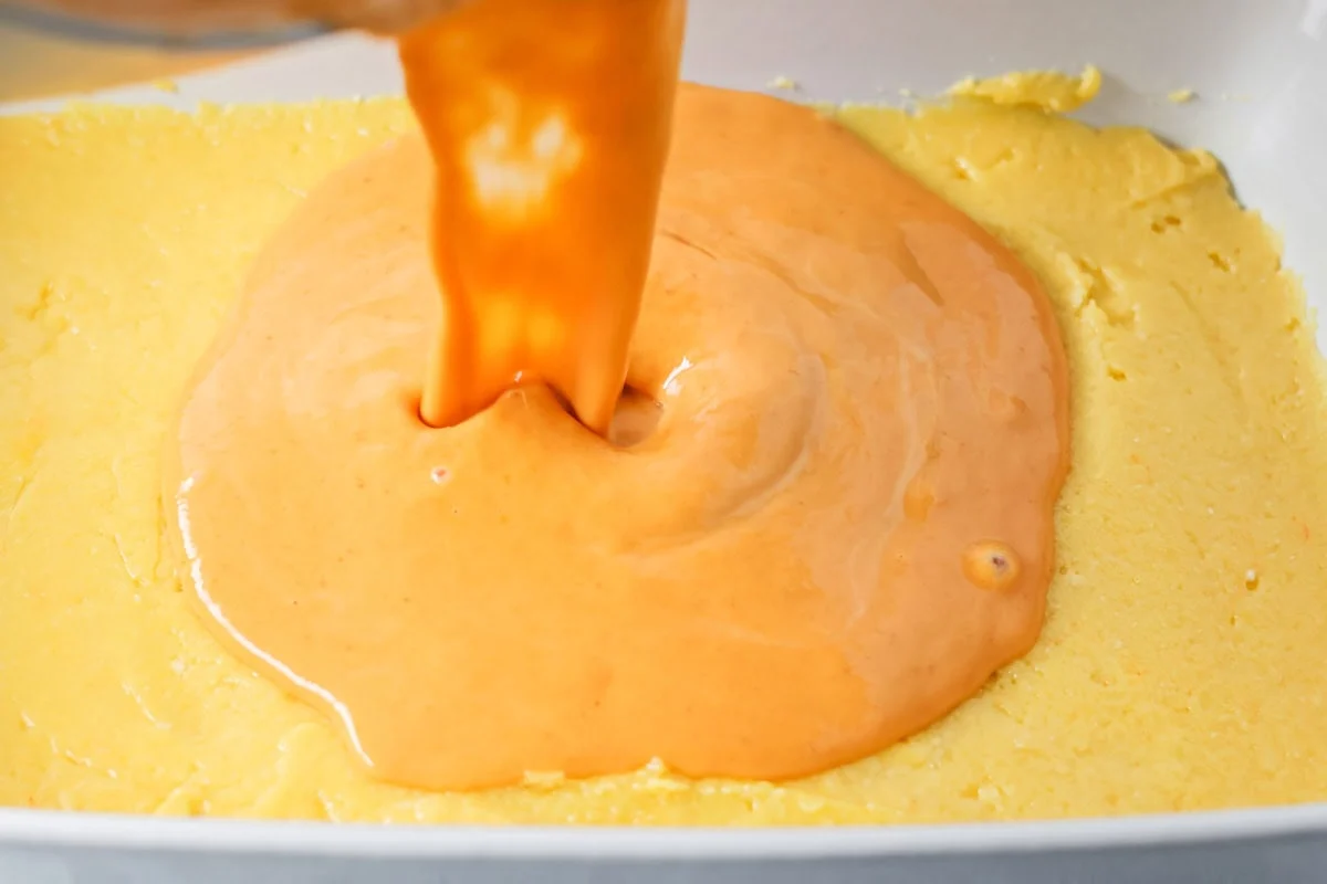 These pumpkin pie bars use a cake mix shortcut to create a fluffy, pumpkin-spiced treat that's perfect for sharing! Pouring pumpkin batter over cake batter.