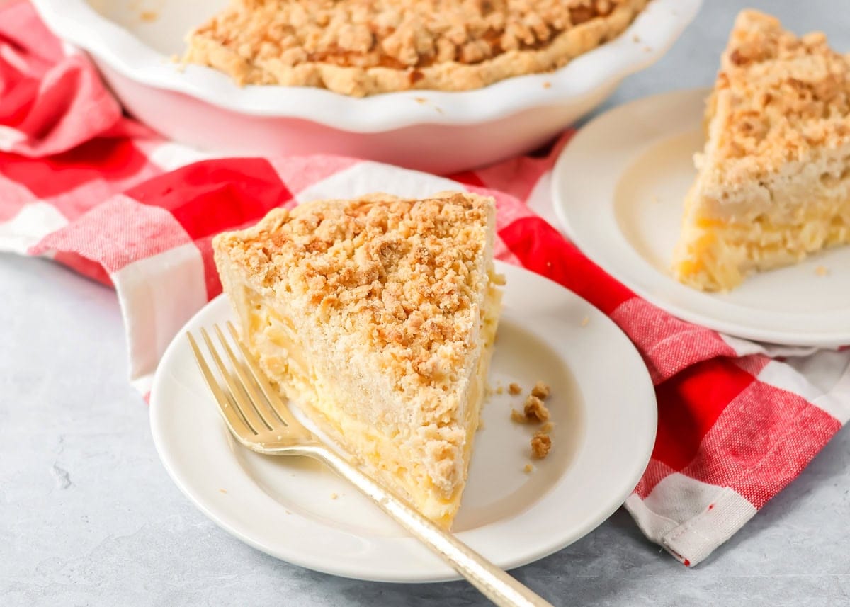 Sour cream apple pie elevates the classic with a rich, tangy, and creamy custard and a buttery crumb topping! A slice of sour cream apple pie on a white plate.